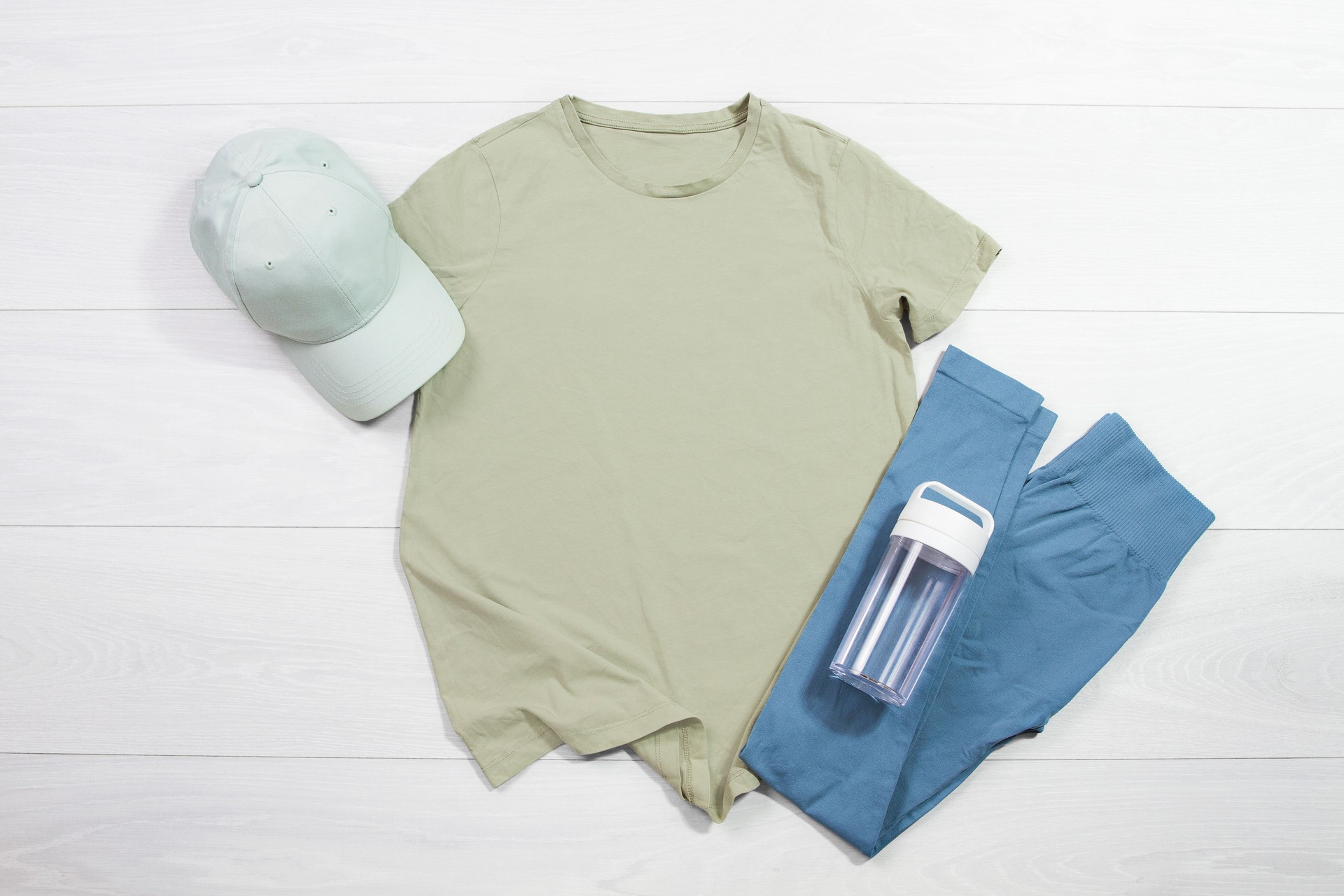 Khaki female sport fitness t shirt mockup flat lay on wooden background. Summer pilates stretching accessories. Sporty leggins, hat. Top front view t-shirt.T-shirt Template blank copy space